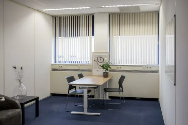 Vergaderruimte aan de Markerkant 13 met een tafel, vier stoelen, een plant en een kunstposter.